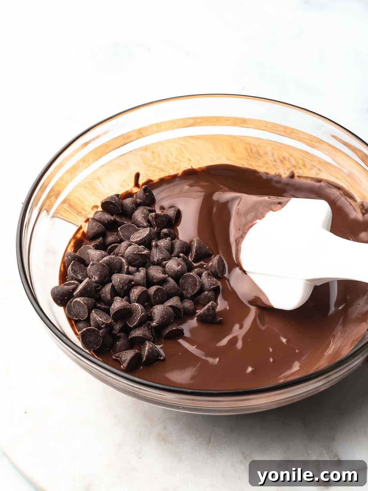 Mastering Chocolate Melting 6 Partially melted chocolate in a microwave-safe bowl, showing chips and liquid chocolate.
