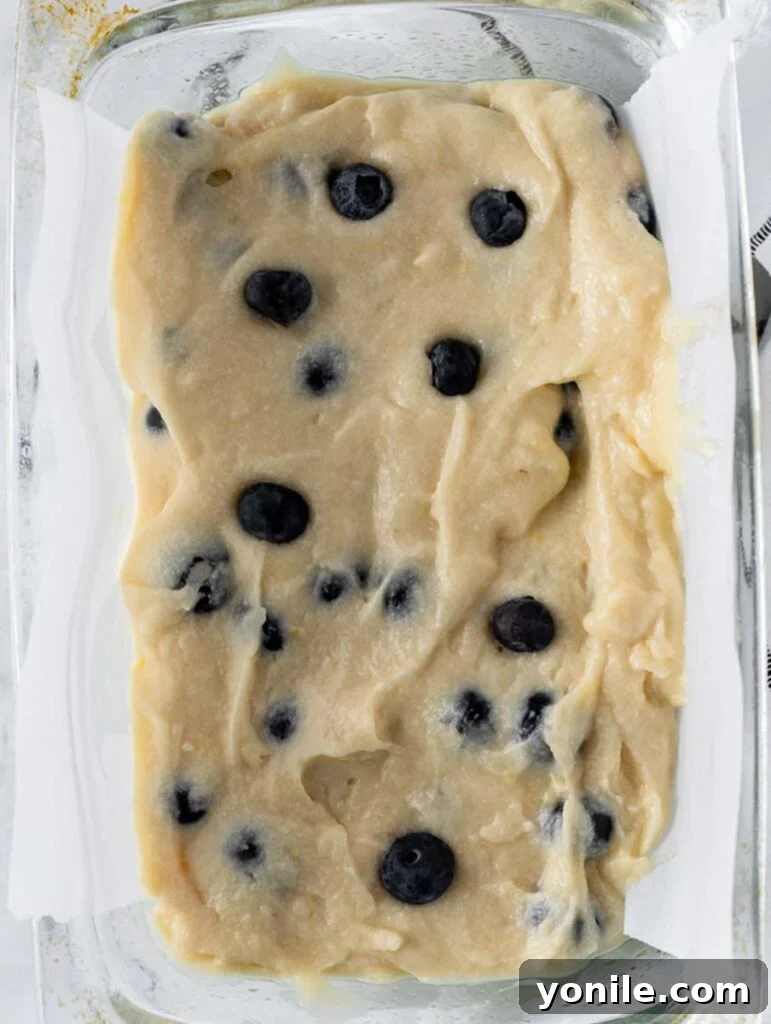 Bright Lemon Blueberry Bread 4 Top-down view of vibrant lemon blueberry bread batter evenly spread in a prepared loaf pan, ready for baking.