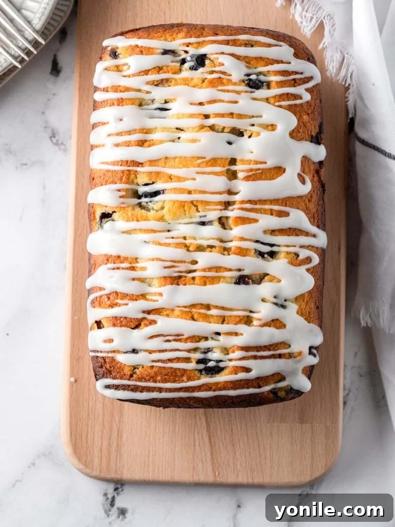 Bright Lemon Blueberry Bread 5 A freshly baked Lemon Blueberry Bread loaf, beautifully glazed with a bright lemon drizzle, presented from a top-down perspective.