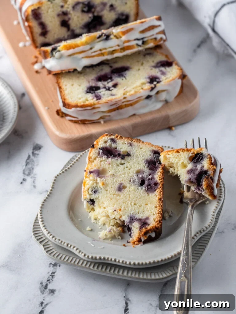 Bright Lemon Blueberry Bread 7 A mouth-watering slice of Lemon Blueberry Bread on a white plate, with a fork gently taking a bite, highlighting its fluffy texture and juicy blueberries.