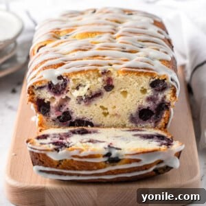 A perfectly sliced homemade Lemon Blueberry Bread, showcasing its moist interior packed with vibrant blueberries and a delicate lemon glaze.