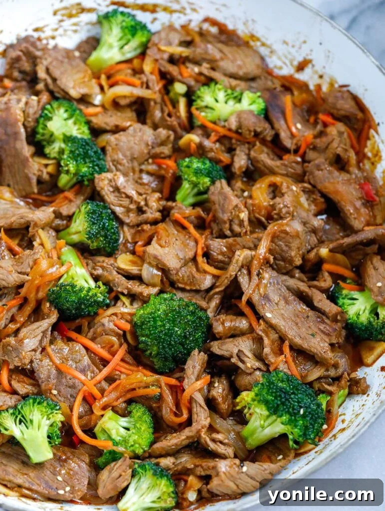 overhead shot of Beef and Broccoli Stir Fry in a white bowl, garnished with sesame seeds