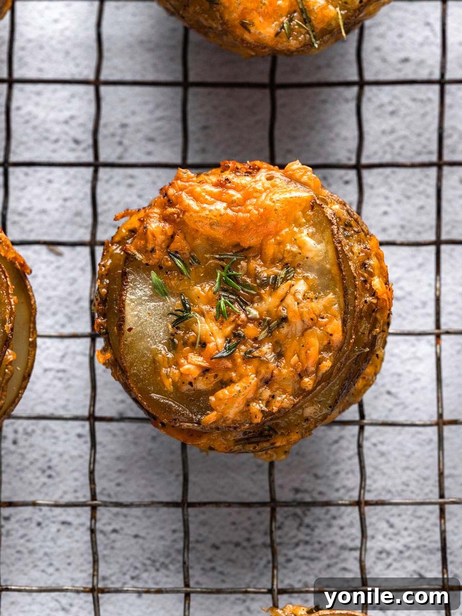 Close-up of golden-brown cheesy potato stacks cooling in a muffin tin.