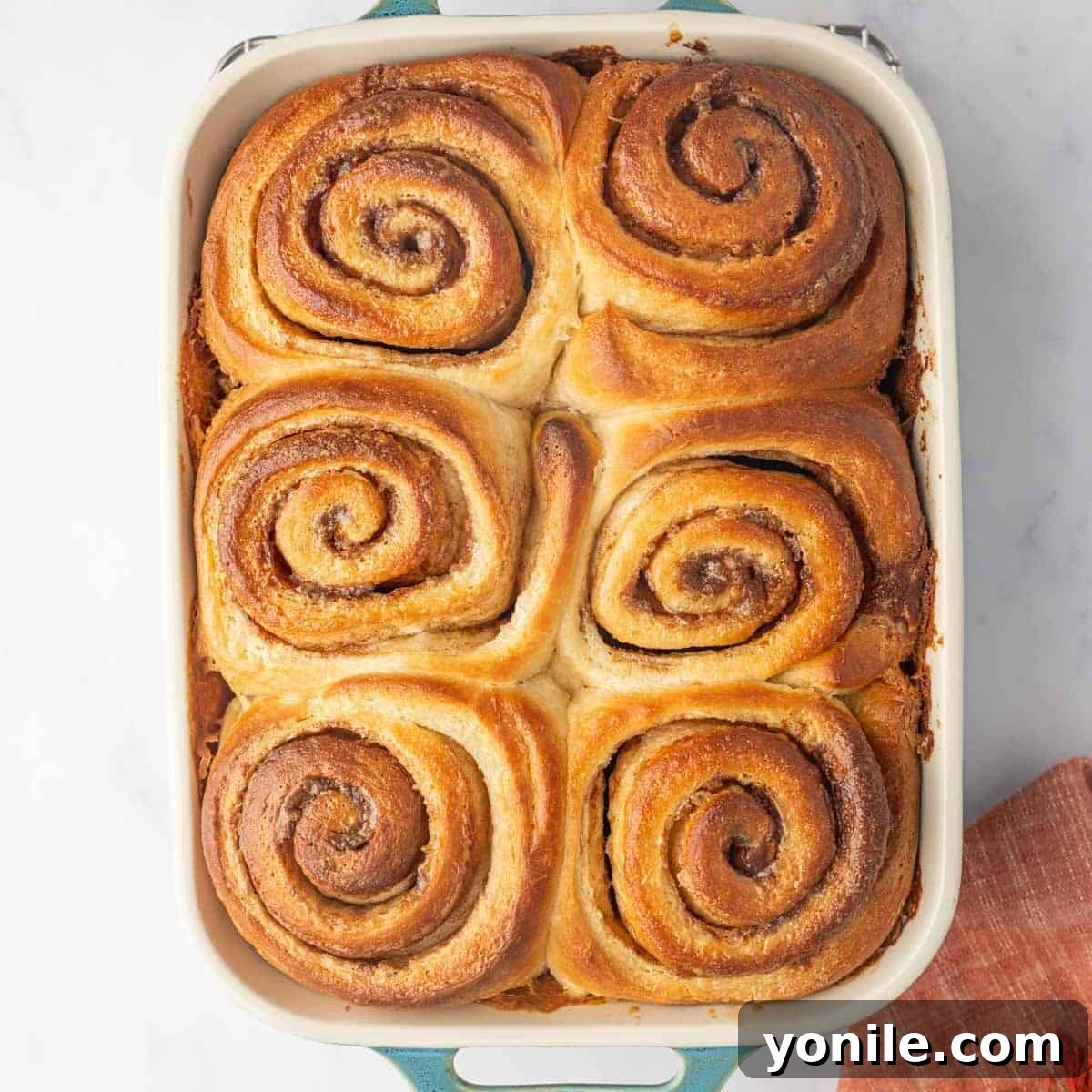 Freshly baked, golden brown cinnamon rolls, still warm and unfrosted, in a rectangular baking dish, showing their soft centers.