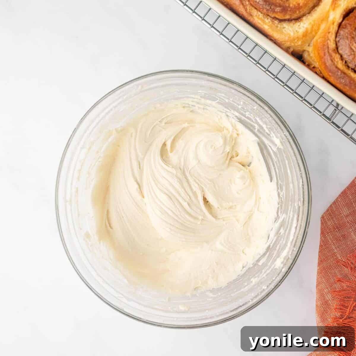 Smooth, creamy cream cheese frosting for cinnamon rolls is prepared and held in a clear glass bowl, ready to be drizzled.