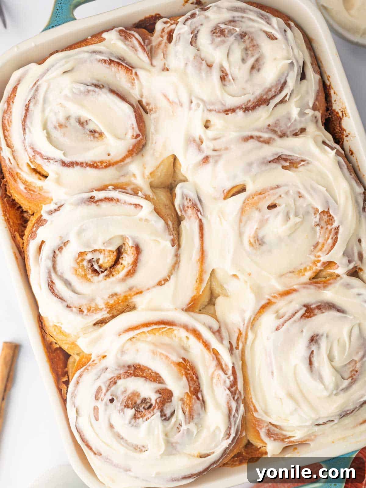 Warm, freshly baked heavy cream cinnamon rolls generously spread with sweet cream cheese frosting in a glass baking dish, ready to be served.