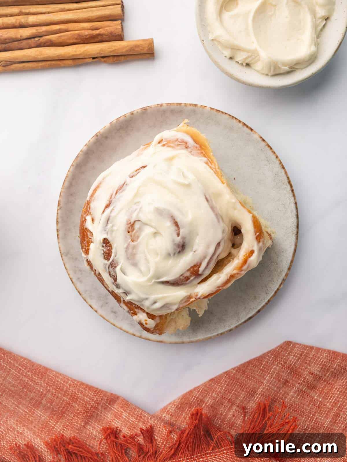 A single, perfectly baked and frosted cinnamon roll, adorned with generous cream cheese icing, served on a white plate, highlighting its soft swirl.