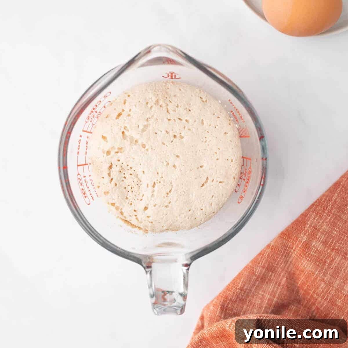 Active dry yeast is proofed in a clear glass measuring cup with warm milk and sugar, showing a foamy top layer.