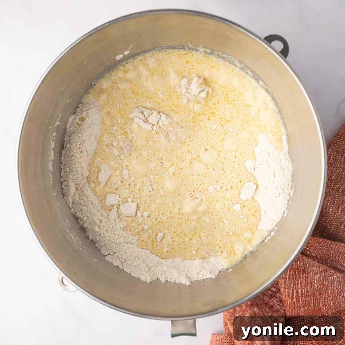 Wet ingredients (yeast mixture, eggs, melted butter) are slowly added to the dry ingredients in a stand mixer bowl.
