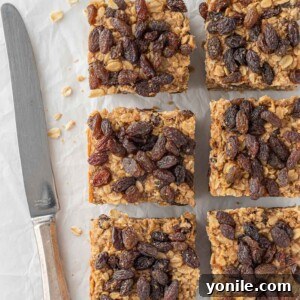 A knife rests beside six cut cinnamon raisin oatmeal bars, highlighting their soft texture.