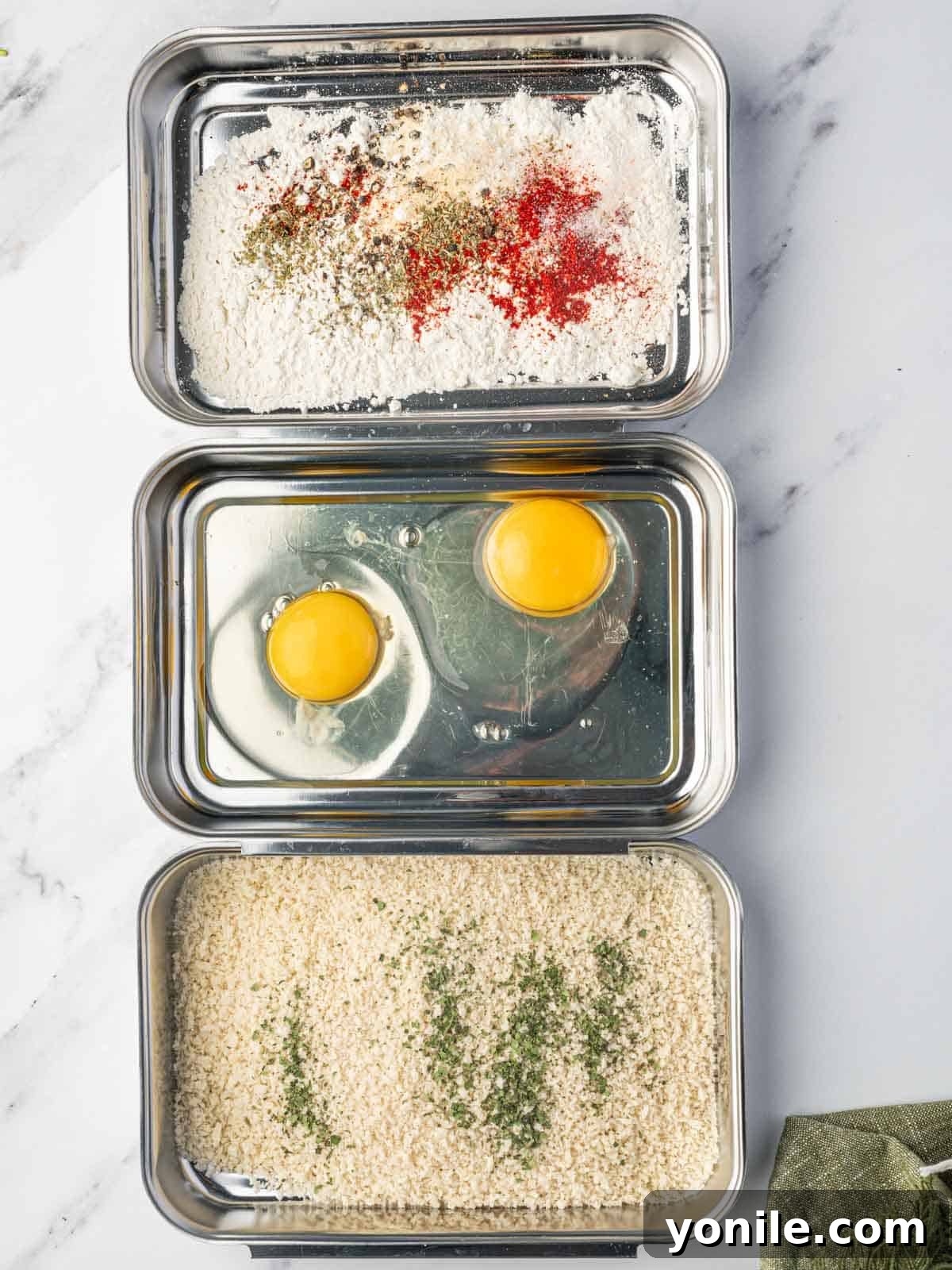 Breading stations for crispy baked cod, showing three bowls with flour, egg wash, and panko mixture.