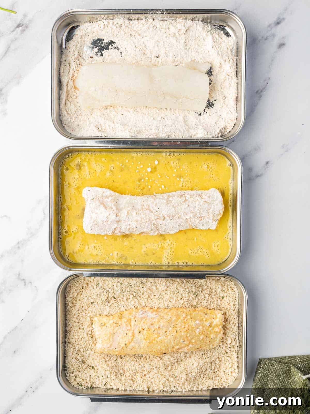 Process of dredging cod fillets in flour, then egg, and finally breadcrumbs for a crispy crust.
