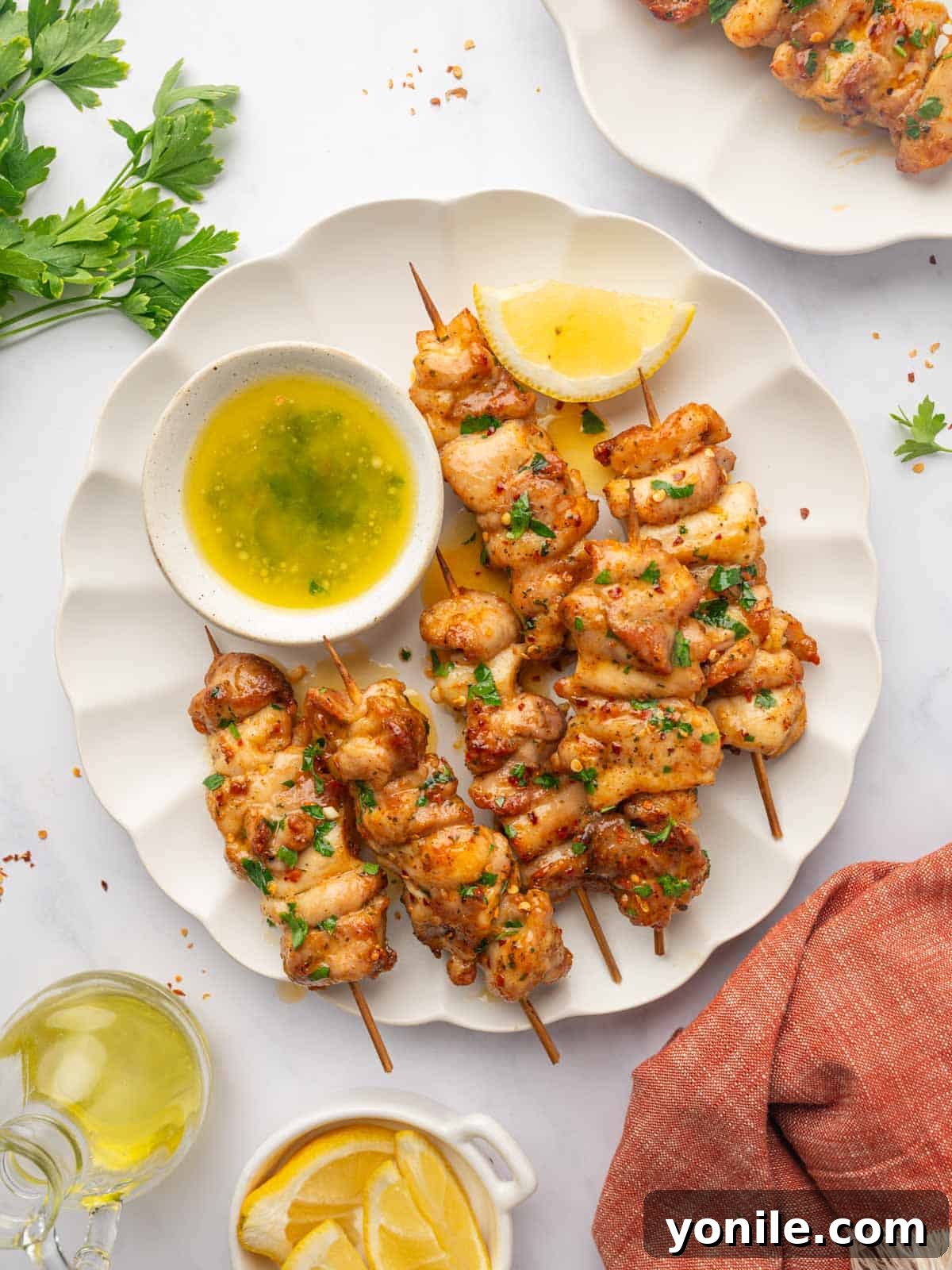 Golden Brown Air Fryer Chicken Skewers on White Plate with Fresh Parsley and Lemon Wedges.