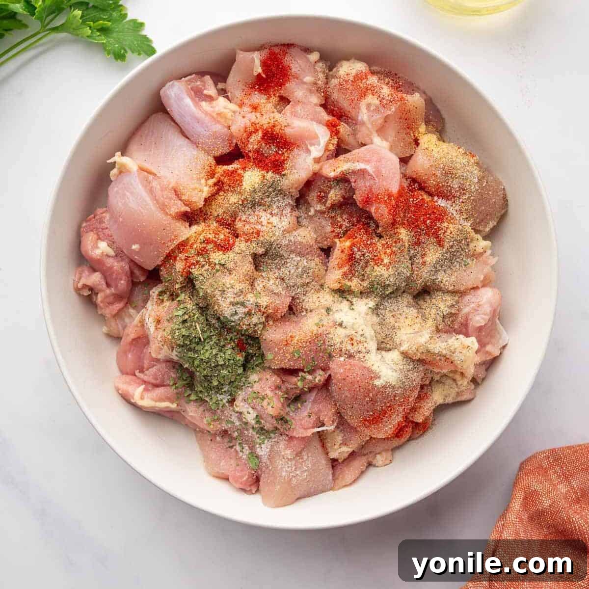 Cubed chicken thighs are seasoned in a bowl.