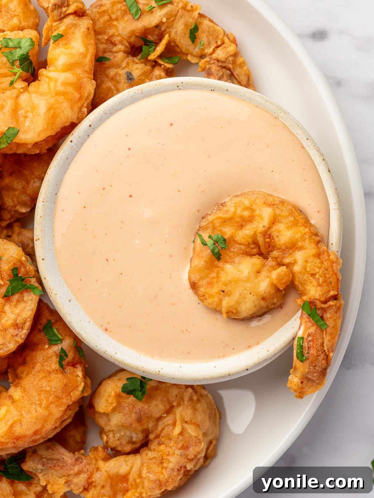 A piece of fried shrimp is dipped into a flavorful sauce.