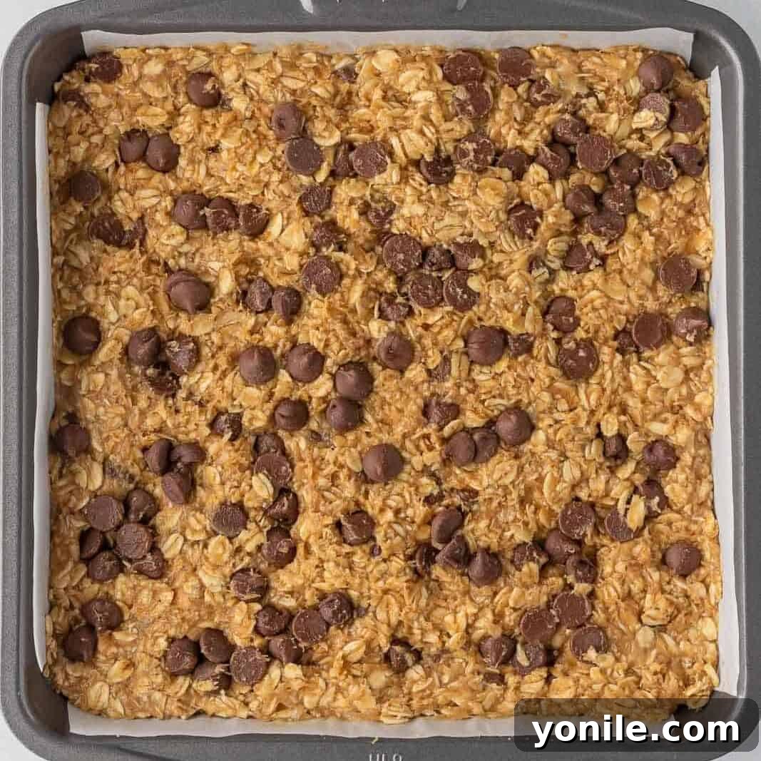 Chewy Chocolate Chip Peanut Butter Oatmeal Bars 5 Uncooked oatmeal bar batter pressed into a square baking pan lined with parchment.